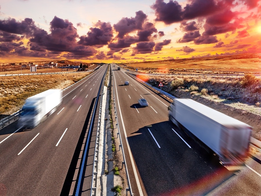 Mehrere Autos und Lastwagen fahren auf einer mehrspurigen Autobahn bei Sonnenuntergang unter einem dramatischen Himmel mit verstreuten Wolken, der die dynamische Welt der Suche nach Führungskräften im Bereich Transport und Logistik symbolisiert.
