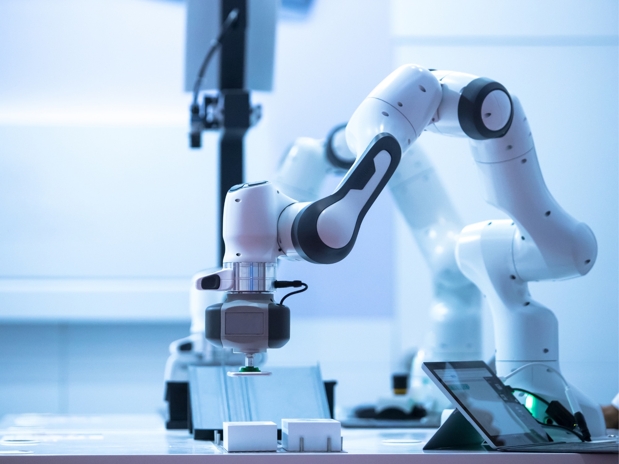 Ein Roboterarm arbeitet auf einer Werkbank und interagiert mit einem Touchscreen und anderen kleinen Objekten in einem modernen, hell erleuchteten Labor - ein ideales Bild für Fachkräfte im Bereich Elektronik und Halbleiter, die auf der Suche nach Innovationen sind.