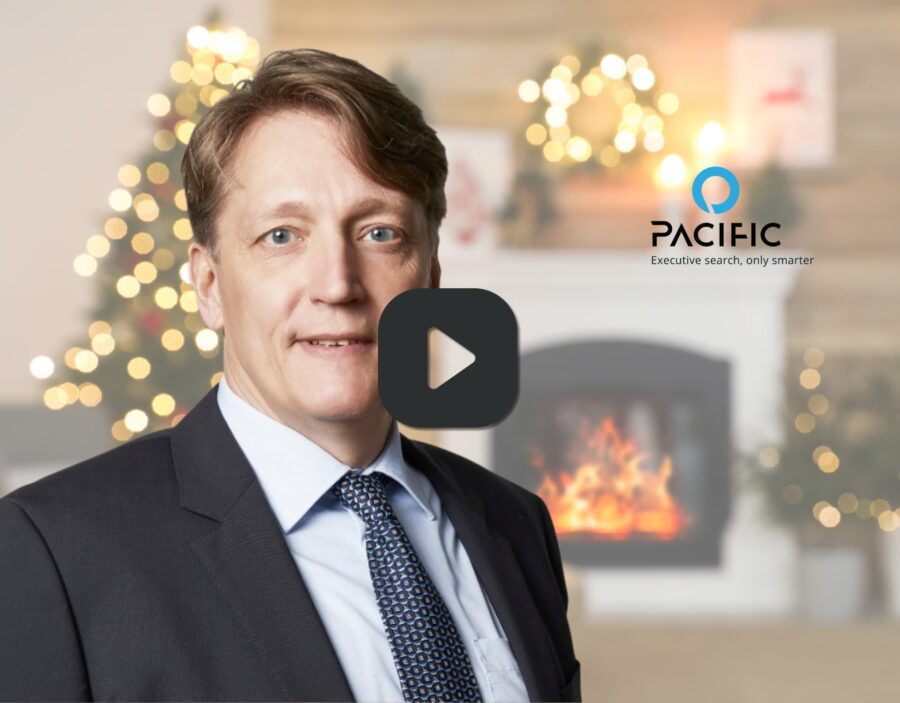 A man in a suit stands in front of a decorated fireplace with a Christmas tree; the Pacific company logo is visible in the background.
