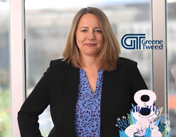 A woman in business attire stands in front of a window, with the Greene Tweed logo and "8 March" graphic in the foreground, marking International Women's Day.